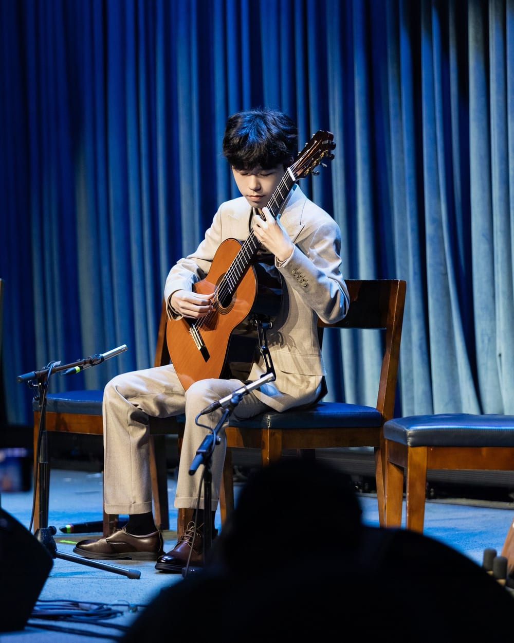 Yuze Pan seated on the stage of Blue Note Beijing, playing the classical guitar.