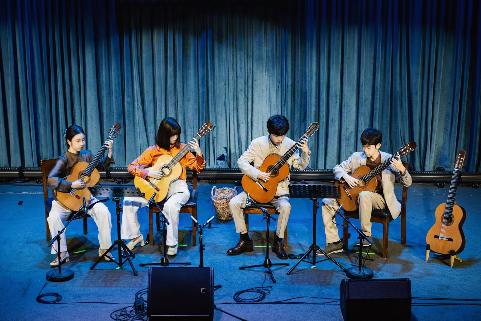 The four players of Primal Guitar Quartet performing on classical guitars on the stage of Blue Note Beijing, a music stand before each of them and a blue velvet curtain behind.